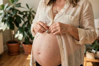 Femme enceinte tenant un bola de grossesse en argent contre son ventre arrondi dans un salon chaleureux aux tons naturels
